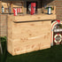 A rustic wooden garden bar made from reclaimed timber, set against an outdoor backdrop with a brick wall and greenery.
