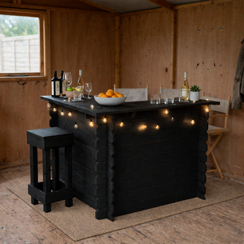 Black wooden bar with string lights in a rustic room with a window and chair.