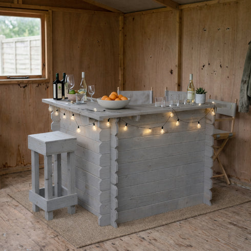 Outdoor bar setup with bottles, fruit, and string lights in a wooden shed.