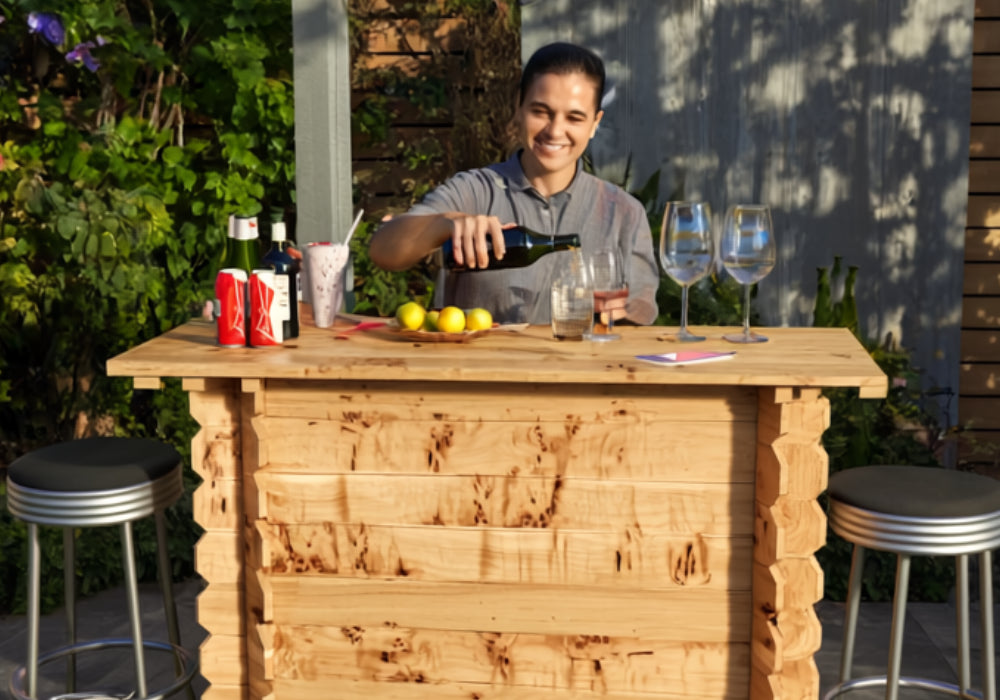 Person pouring wine at a wooden outdoor bar with stools and bottles.