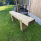 A rustic wooden garden bench made from natural timber, positioned on a green grass lawn next to a wooden fence.