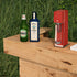 Bottle of Carambar and Bombay Sapphire gin with a red soda machine on a wooden table outdoors.