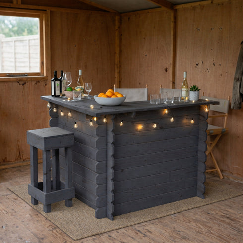 Indoor bar setup with a gray wooden bar, stools, and decorative lights in a wooden shed.
