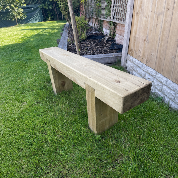 A rustic wooden garden bench made from natural timber, positioned on a green grass lawn next to a wooden fence.