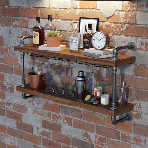 Wooden bar shelf with bottles, glasses, and a clock against a brick wall.