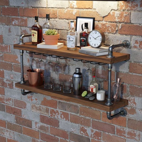 Wooden bar shelf with bottles, glasses, and a clock against a brick wall.