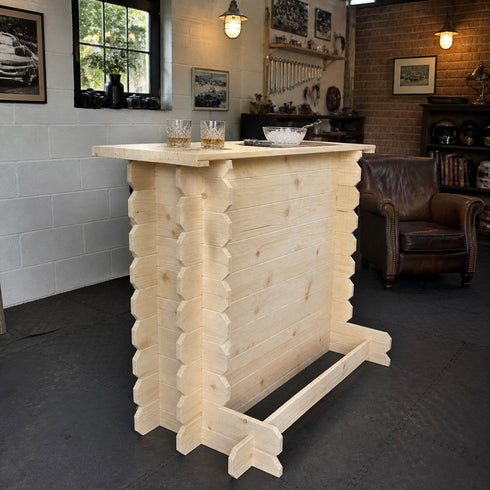 A light natural wood log-style bar table with a rustic cabin aesthetic, shown in a workshop or home bar setting with stools and brick walls in the background.