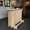 A light natural wood log-style bar table with a rustic cabin aesthetic, shown in a workshop or home bar setting with stools and brick walls in the background.