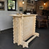 A light natural wood log-style bar table with a rustic cabin aesthetic, shown in a workshop or home bar setting with stools and brick walls in the background.