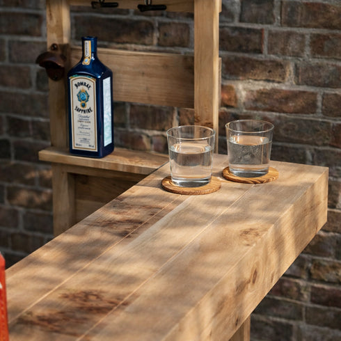 Bottle of Bombay Sapphire gin with two glasses on a wooden surface against a brick wall.