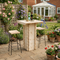 Outdoor patio setup with wooden bar table, stools, and potted plants in a garden.