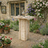 Wooden garden table with tea set surrounded by flowers and plants in a garden setting.